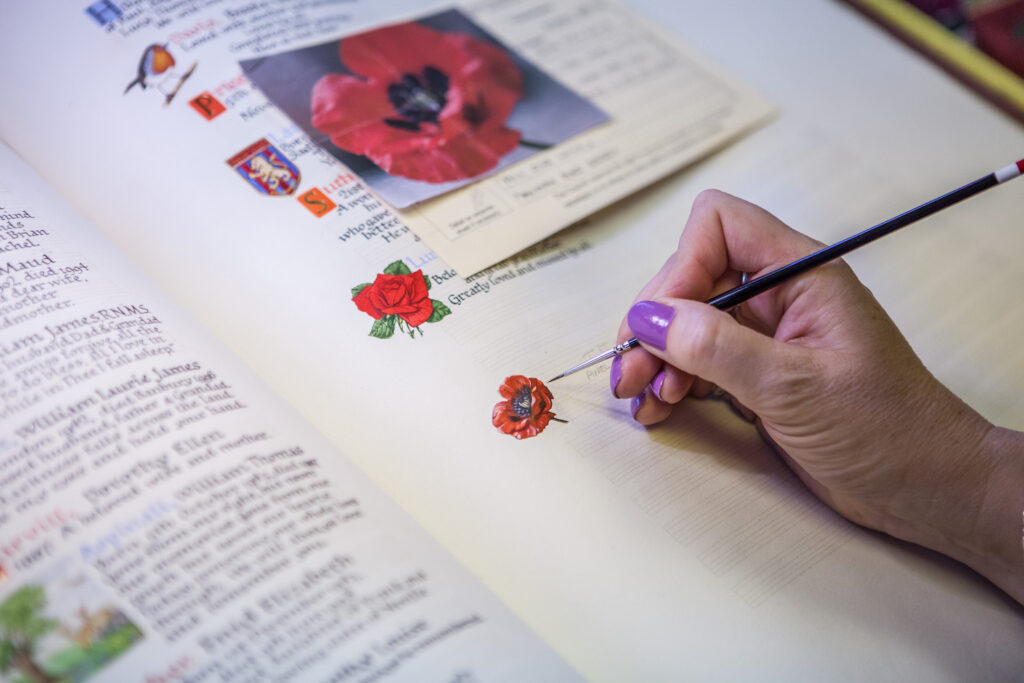 Hand painting a red poppy flower onto the Book of Remembrance