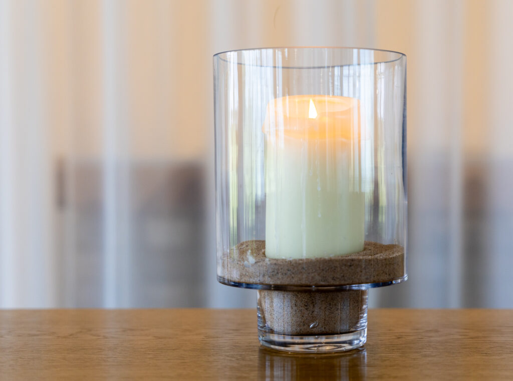 Ivory wax candle placed inside a glass candle holder, on a raised base